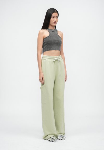 Szary prążkowany crop top z wysokim dekoltem, zestawiony z jasnoszarymi spodniami dresowymi o szerokich nogawkach, które mają kieszeń boczną i sznurek do regulacji. Srebrne szpiczaste buty.