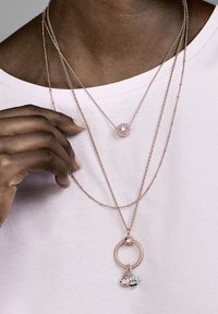 Collane a strati con catene in oro rosa. Un pendente con pietre rosa, un altro con un charm a forma di ape in argento, formando un design delicato.