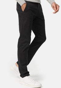Black chinos made of cotton with a smooth texture, slim fit, side pockets, and a clean design, paired with white sneakers.