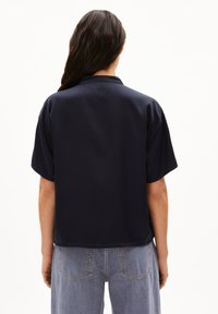 Kurzärmliges, navy-blaues Shirt aus glattem Stoff mit einem lässigen Kragen und Rückendetail, kombiniert mit hellgrauen weit geschnittenen Jeans.