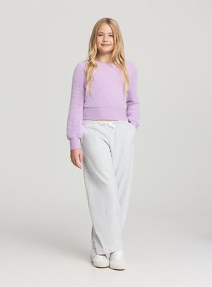 Maglione corto lilla peloso con polsini a costine abbinato a pantaloni della tuta grigio chiaro con cintura elastica in vita. Scarpe da ginnastica bianche completano il look.