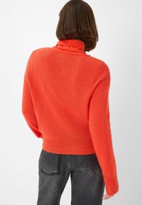 Helles orange cropped Sweater mit einer weichen, strukturierten Oberfläche. Verfügt über einen hohen Ausschnitt und lange Ärmel, kombiniert mit dunkelgrauen Jeans.