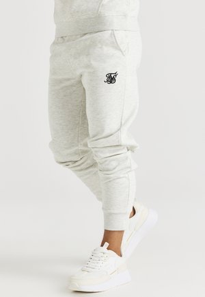 Lichtgrijze sweatpants van zachte stof, met een zwart logo op de dij, taps toelopende boorden en zijzakken. Gecombineerd met witte sneakers.
