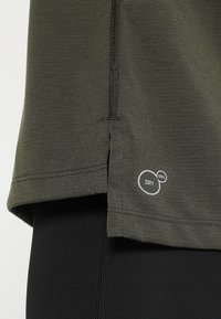 Olivgrön träningströja med rundad nederkant, fuktabsorberande teknikmärke längst ner, sydda sömmar och mjuk textur.