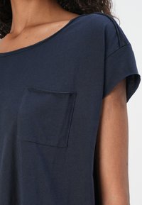Chemise bleu marine à col rond, à manches courtes et avec une poche à l'avant. Texture douce et coupe décontractée, avec des détails d'épaule sans couture.