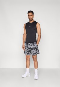 Μαύρο αθλητικό τοπ χωρίς μανίκια με λευκό λογότυπο Nike, συνδυασμένο με γκρι σορτς καμουφλάζ με μαύρα και λευκά σχέδια. Λευκά αθλητικά παπούτσια και κάλτσες.