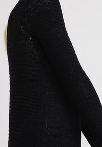 Schwarzer, gestrickter Pullover mit lockerem Maschenbild, langen Ärmeln und lockerem Schnitt, der eine strukturierte Oberfläche zeigt.