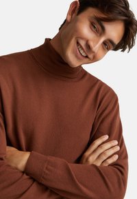 Brązowy sweter z golfem, wykonany z miękkiego materiału, z długimi rękawami i prążkowanymi mankietami, o luźnym kroju i minimalnej teksturze.