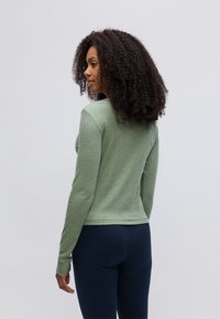 Strakke groene langemouwen top met een gestructureerde afwerking, ronde halslijn en geribde manchetten, gecombineerd met donkerblauwe onderkleding.