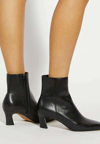 Bottes noires en cuir à la cheville avec un design épuré, un orteil pointu et un petit talon épais ; dotées d'une fermeture éclair sur le côté pour un enfilage facile.