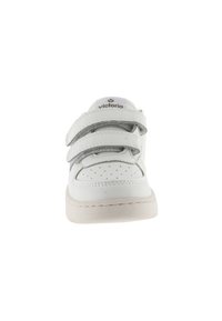 Sneaker blanche avec trois bandes Velcro, design perforé à la pointe, texture en cuir lisse et semelle beige discrète. Logo de la marque sur la languette.