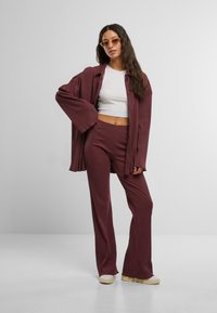 Chemise en maille côtelée bordeaux avec des fermetures à boutons et des manches larges, associée à un pantalon côtelé assorti, doté d'une taille ajustée et de jambes évasées.