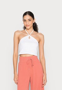 Top crop halter branco com detalhe em forma de buraco, combinado com calças jogger corais soltas que apresentam uma cintura elástica e cordão. Textura suave.