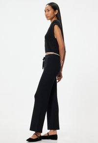 Zwarte geribbelde gebreide crop top met korte mouwen, gecombineerd met zwarte high-waisted brede broek, met een trekkoord in de taille en platte schoenen.