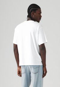 T-shirt bianco a maniche corte in cotone, con collo a giro e vestibilità rilassata. Sul retro presenta una superficie liscia senza grafiche.