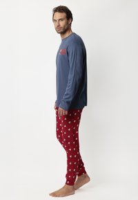 Camisa de manga larga azul con texto rojo, combinada con pantalones de pijama rojos que presentan un patrón de osos blancos. Tejido suave con un diseño ajustado.