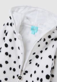 Weißer Fleece-All-in-One mit schwarzen Punkten, ausgestattet mit Kapuze, Frontreißverschluss und einem Reißverschluss-Anhänger in Form einer Pfote. Weicher Stoff und verspieltes Design.