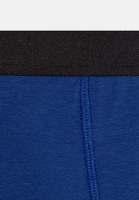 Modré bavlněné boxerky s černým pružným pasem a viditelným šitím podél švu pro větší trvanlivost a lepší přizpůsobení.