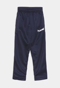 Marina atletiska byxor i slätt tyg, med elastisk midja och en vit logotyp på vänstra låret. Korta i längden.