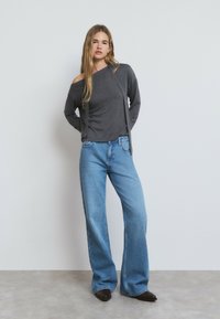 Haut gris à manches longues avec un design décolleté, associé à un jean évasé bleu clair. La tenue présente une coupe décontractée et une texture lisse.