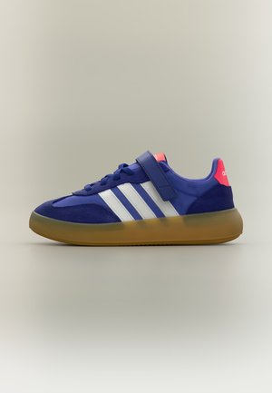 Синя маратонка Adidas с бели ивици, гумена подметка, розов козирка на петата, връзки и велкро лента отгоре в страничен изглед на неутрален фон.