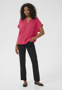 Blouse rose à manches courtes avec décolleté en V et coupe décontractée, associée à un pantalon noir à jambes droites et des ballerines noires. Finition textile lisse.