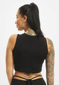 Čierny skrátený top bez rukávov, vyrobený z jemnej bavlny. Viditeľné tatto na ramene a chrbte. Minimalistický štýl.