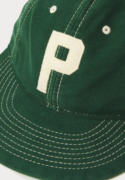Capa de tecido verde com um proeminente emblema em creme com a letra "P". Apresenta costura branca e buracos de ventilação na coroa.