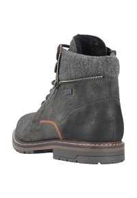 Botte cheville en suede gris foncé avec un col en textile gris texturé, présentant un accent marron et une fermeture éclair en métal. Semelle en caoutchouc robuste pour une bonne adhérence.