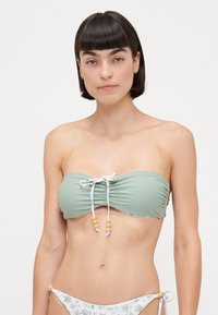 Svetlozelena bandeau bikinka s nabrane tkanine, ima vezivanje ukrašeno drvenim perlama. Bikini donji dio s uzorkom cvijeća.