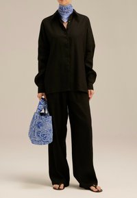 Czarna lniana koszula i spodnie o szerokich nogawkach, do których dobrano niebieską torebkę w wzór paisley oraz pasującą chustę. Całość dopełniają płaskie sandały.