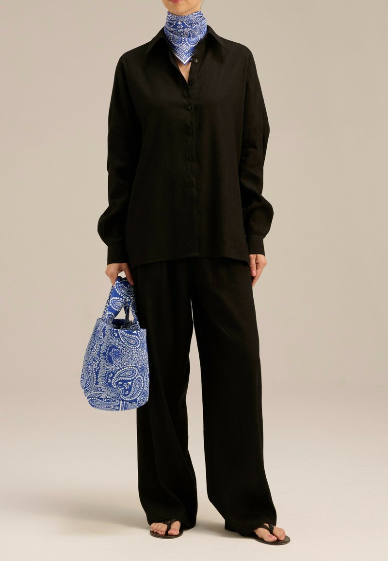 Czarna lniana koszula i spodnie o szerokich nogawkach, do których dobrano niebieską torebkę w wzór paisley oraz pasującą chustę. Całość dopełniają płaskie sandały.