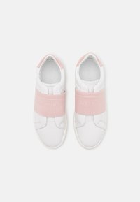 Baskets blanches à enfiler avec larges bandes élastiques roses sur le dessus et accents roses au talon, arborant le logo Calvin Klein sur les bandes.