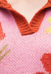 Πλεκτό πουλόβερ με ροζ σώμα, διακοσμημένο με λουλουδάτα μοτίβα σε πορτοκαλί, κίτρινο και πράσινο - λαιμόκοψη σε σχήμ�α V με πορτοκαλί υφή και απαλό ύφασμα.