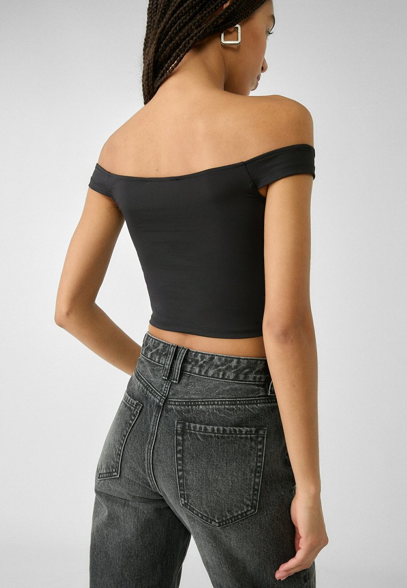 Top nero a maniche scese, in tessuto elasticizzato, abbinato a jeans in denim scuro a vita alta con una finitura testurizzata e tasche posteriori.