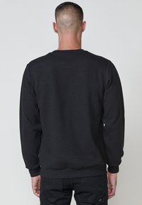 Sudadera negra con tejido texturizado, puños y dobladillo de canalé. Diseño sencillo con escote redondo. Visto desde la parte de atrás.