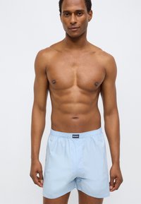 Ανοιχτό μπλε μαγιό με ελαστική μέση και μπροστινή πατιλέτα. Κατασκευασμένο από ελαφρύ, ομαλό υλικό. Χωρίς σχέδια ή μεταλλικά στοιχεία.