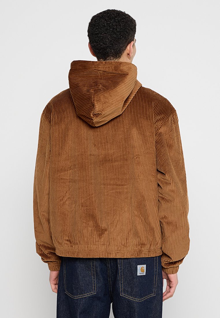 Chaqueta con capucha de pana marrón con textura acanalada, ajuste holgado y puños elásticos. Presenta una capucha y un dobladillo en la parte inferior.