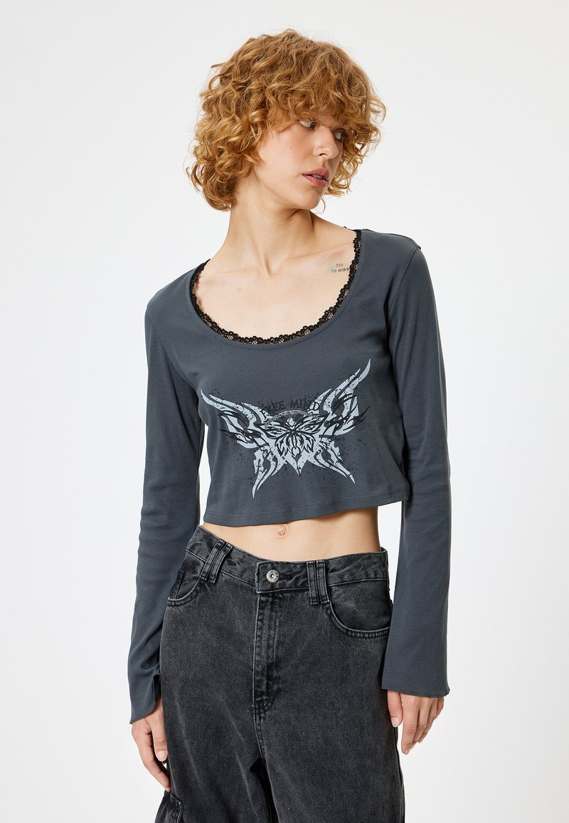 Gekürztes Langarmshirt aus dunkelgrauer Baumwolle mit einem schwarzen Spitzenbesatz am Kragen und einem grauen Grafikdesign auf der Vorderseite.