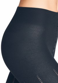 Schwarze, gerippte Leggings mit einem hohen Bund, glatter Textur und dekorativen Ausschnitten entlang des Unterschenkels.
