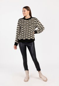 Zwarte en crèmekleurige gebreide trui met een gestructureerd patroon, gecombineerd met strakke zwarte legging en beige enkelboots met een chunky zool.