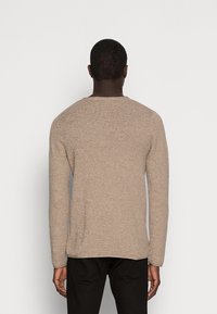 Beige långärmad tröja med en texturerad stickad mönster, rund halsringning och rak passform. Bärs med svarta byxor. Enkelt design.