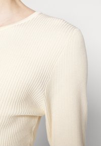 Maglione a coste color crema con scollatura rotonda e maniche lunghe, che presenta un tessuto testurizzato con linee verticali.
