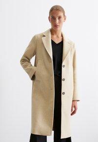 Hellbeige Wollmantel mit taillierter Passform, Reverskragen, zwei Vorderfächern und drei Knöpfen auf der Vorderseite. Geschmeidige, weiche Textur.