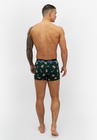 Gröna kalsonger med ett mönster av pepparkaksgubbar och jultikar, med ett marinblått resårmidjeband märkt "GLADA SHORTS."