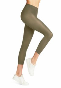 Leggings verde oliva realizzati in un materiale elastico e liscio. Design aderente con vita media. Indossati con sneakers bianche.