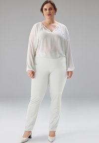 Blouse blanche à manches longues avec un décolleté incurvé, associée à un pantalon slim blanc et des talons blancs. Tissu lisse, détails minimalistes.