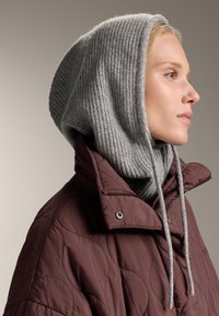 Burgundiszínű steppelt dzseki magas gallérral, szürke bordázott kötött kapucnival párosítva. Állítható zsinórokkal és texturált felülettel rendelkezik.