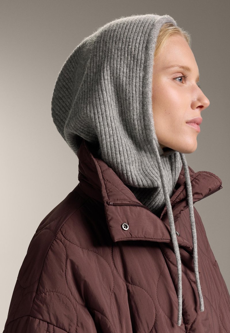 Burgundiszínű steppelt dzseki magas gallérral, szürke bordázott kötött kapucnival párosítva. Állítható zsinórokkal és texturált felülettel rendelkezik.