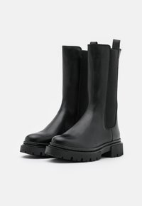 Mustat nahkaiset nilkkabootsit, joissa on joustavat sivupaneelit, paksu kumipohja ja sileä pinta. Varustettu silmukoilla, jotka helpottavat pukemista.